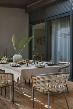 Terasın iç tasarımı bahçe koltuğu, yastıklar, çiçekli vazo örülmüş sepet, ekose, büyük pencere, kase, ahşap zemin ve kişisel aksesuarlarla. Ev dekoru. Şablon.