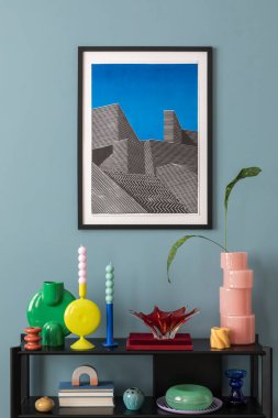 Mavi duvardaki renkli kompozisyon poster çerçevesi, siyah raf, tasarım aksesuarları ve yapraklı vazolar, mumlar. Ev dekoru. Şablon. 