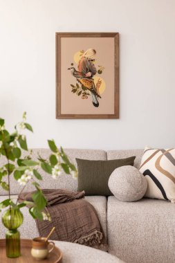 Oturma odasında bej bir kanepe ve desenli yastıklarla süslenmiş. Duvarda bir kuşla bir kadını gösteren çerçeveli bir sanat eseri asılı. Saksı bitkisi ve açık bir kitap dingin atmosfere katkı sağlar..