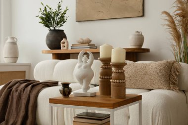 Konforlu ve boho oturma odasında beyaz bir kanepe, desenli yastıklar ve battaniyeler, dekorasyonlu ahşap bir sehpa ve doğal tonda dekoratif elementler var. Şık bir iç mekan. Şablon.