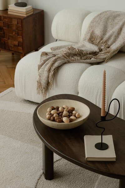 A stylish, minimalist living room area with dark wooden coffee table, candelstick, nuts and elegant decor, soft lighting, and a tranquil ambiance. Home styling. Template.