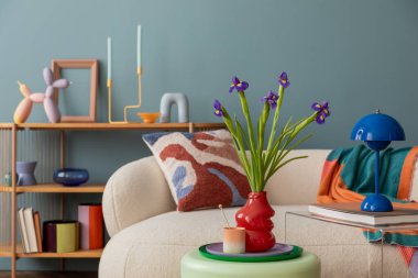 Çağdaş dekoratif aksanlı modern oturma odası. Şablonlu bir yastıkla süslü rahat bir kanepe, canlı vazolar, ve mavi bir lamba, koyu kırmızı bir vazoda taze irislerle tamamlanmış..