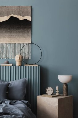 Katmanlı mavi tekstil kaplı rahat bir yatak odası, açık bir kitap ve yumuşak ışıklandırma. Kumaş ve modern dekorun dokunsal bir karışımı sıcak ve davetkar hissi arttırır..