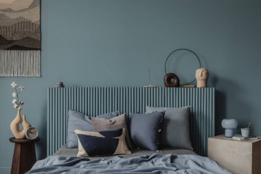 Pamuk saplı minimalist bir yatağın yakın plan çekimi heykel vazosunda, parlak mavi bir lamba ve huzurlu bir okuma köşesi için istiflenmiş kitaplar..