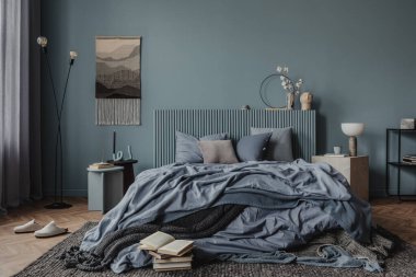 Karmaşık duvar halısı, hafif ahşap aksanlı modern bir yatak odasının geniş bir görüntüsü ve dikkatlice düzenlenmiş kitaplar sıcak ve davetkar bir atmosfer yaratıyor..