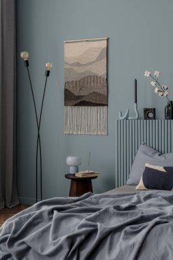 Sade bir yatak odası sahnesi, dokulu duvar halısı, vazoda pamuk sapları, ve katmanlı mavi yatak, doğal tonlara ve rahat dokulara vurgu.