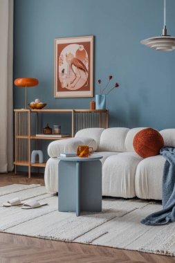 Açık bir oturma odasında bej bir kanepe, duvarlarda çağdaş sanat eserleri ve yumuşak doğal ışıklandırma sergileniyor..