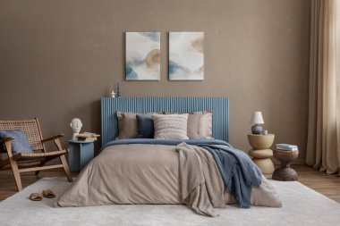 Modern bir yatak odası manzarası, koyu mavi bir yatak başlığı, heykel yan tabloları, ve toprak tonlu dekorlar, çağdaş ve organik elementleri harmanlıyor.