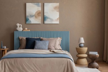 Sakin bir yatak odası, mavi aksanlı yatak başlığı, katmanlı battaniyeler ve organik şekiller, sakinlik ve rahatlık hissi uyandırıyor..