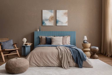 Sıcak ve davetkar bir yatak odası. Doğal ahşap masa, heykel dekoru ve yatağın üstünde soyut resimler var..