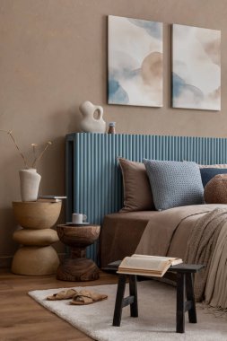 Güzel düzenlenmiş bir yatak odasına yakın çekim. Mavi bir yatak başlığı, dekoratif yastıklar ve sıcak ahşap sehpaları var..