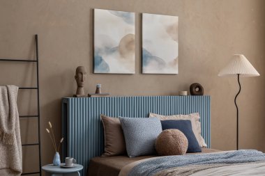 Yumuşak bej ve mavi paletli şık bir yatak odası, desenli bir yatak örtüsü ve heykel dekorasyonu içeriyor..