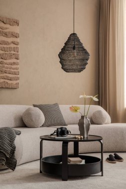 Bej desenli duvarları, desenli kanepesi, siyah sehpası ve kolye lambası olan modern oturma odası. Tarafsız tonlar ve minimalist dekor sakin ve rahat bir atmosfer yaratır.