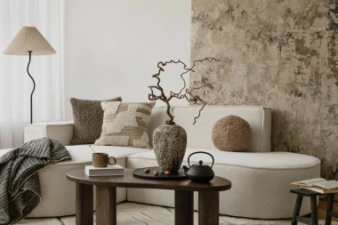 Yumuşak yastıklı, seramik vazosu olan rahat bir oturma odası ve işlenmemiş sanatsal bir arkaplana karşı şekillendirilmiş kurumuş dallar..