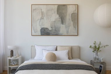 Yumuşak nötr tonları olan parlak minimalist yatak odası yatağın üzerinde büyük soyut resim ve beyaz perdelerin arasından akan doğal ışık..