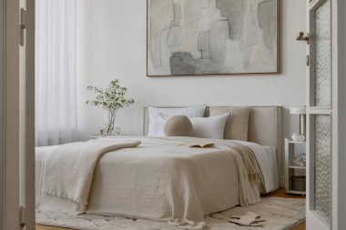 Yumuşak nötr tonları olan parlak minimalist yatak odası yatağın üzerinde büyük soyut resim ve beyaz perdelerin arasından akan doğal ışık..