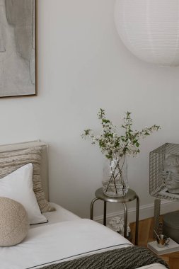 Minimalist bir yatak odasının köşesindeki sehpanın üzerinde çiçek açan dallarla dolu cam vazonun ayrıntıları. Yatak odasının iç tasarımı. 