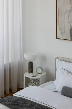 Mermer lambalı komodinin yakın çekimi, modern saat, ve sakin bir yatak odasında dekoratif mercan aksanı..