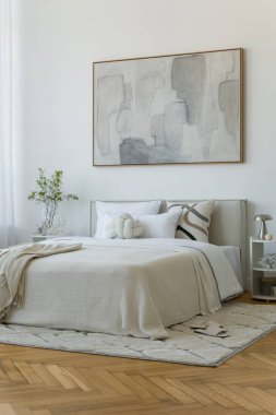 Yumuşak nötr tonları olan parlak minimalist yatak odası yatağın üzerinde büyük soyut resim ve beyaz perdelerin arasından akan doğal ışık..