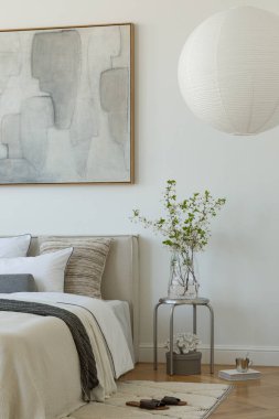 Yumuşak nötr tonları olan parlak minimalist yatak odası yatağın üzerinde büyük soyut resim ve beyaz perdelerin arasından akan doğal ışık..