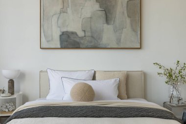 Yumuşak nötr tonları olan parlak minimalist yatak odası yatağın üzerinde büyük soyut resim ve beyaz perdelerin arasından akan doğal ışık..