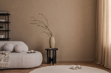 Modern mobilyaları olan minimalist bej bir iç mekan, siyah bir masada seramik bir vazo ve doğal dokuları ve sıcak nötr tonlarıyla biçimlendirilmiş yumuşak yuvarlak bir halı..