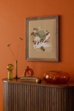 Zarif poster çerçevesi sıcak tonlu dekoratif aksanlar, kişisel aksesuarlar ve kitap eşleştirilmiş..
