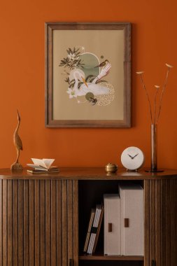 Poster sanatı, ahşap dolap ve turuncu duvara dayalı minimalist aksesuarlar ile dekoratif düzenleme.