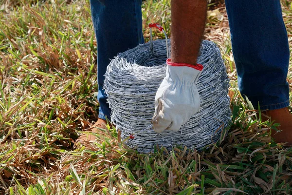 A man s hands manipulate rolls of barbed wire with glove. Barbed wire is used to make fences, protect property, and make borders to show the area\'s territory.