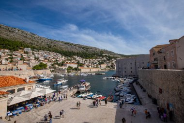 Dubrovnik, Hırvatistan - Ekim 05, 2022 - Eski şehir duvarı (ortaçağ Ragusa) ve Adriyatik Denizi 'nin Dalmaçya kıyılarından liman manzarası. Bağlı tekneler ve turistler geziniyor. Dubrovnik, Hırvatistan
