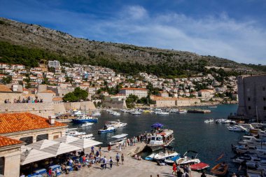 Dubrovnik, Hırvatistan - Ekim 05, 2022 - Eski şehir duvarı (ortaçağ Ragusa) ve Adriyatik Denizi 'nin Dalmaçya kıyılarından liman manzarası. Bağlı tekneler ve turistler geziniyor. Dubrovnik, Hırvatistan