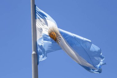 Güneşli bir günde mavi gökyüzünde bayrak direğinde dalgalanan Arjantin bayrağı. Arjantin 'in vatanseverlik sembolü