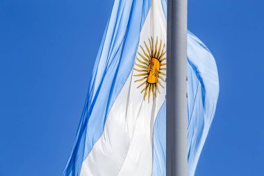 Güneşli bir günde mavi gökyüzünde bayrak direğinde dalgalanan Arjantin bayrağı. Arjantin 'in vatanseverlik sembolü