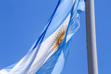 Güneşli bir günde mavi gökyüzünde bayrak direğinde dalgalanan Arjantin bayrağı. Arjantin 'in vatanseverlik sembolü