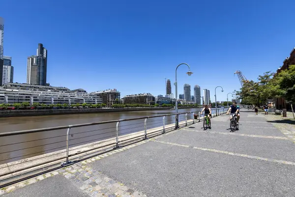 Buenos Aires, Arjantin 27 Ocak 2024 - Puerto Madero, modern binaların mimarisi, yeniden canlandırılmış bir yer ve turistler tarafından ziyaret ediliyor. Bisikletçiler güzel şehir manzarasında gezerler..