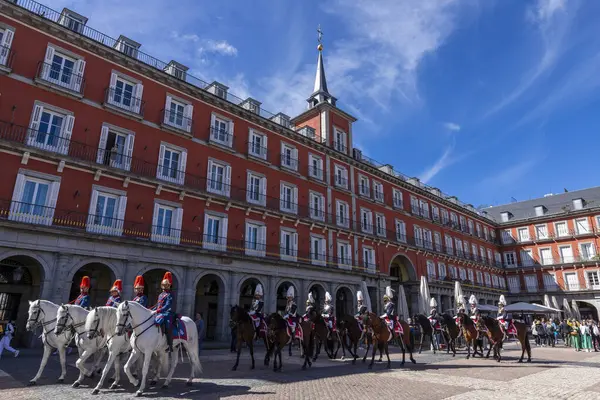 stock image Madrid, Spain - April 08, 2024: Military men and women in ceremonial uniform and mounted on horses, participate in a parade, watched by tourists on a sunny day in the Plaza Mayor.