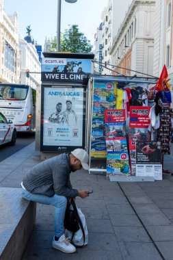 Madrid, İspanya - Nisan 09, 2024 Madrid 'deki Gran' de İspanya vatandaşı gazete bayiinin yanındaki cep telefonuna bakar.