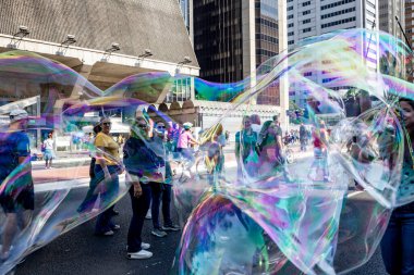 Sao Paulo, Brezilya - 28 Haziran 2024 - Paulista Bulvarı 'nda hava kabarcıkları üfleyen sokak sanatçısı, güneşli bir yaz gününde turistler etrafta geziniyor.