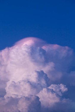 Massive cloud colored in shades of pink and purple with a deep blue sky background clipart