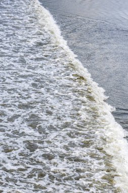 Kumlu bir kıyıda yumuşak bir dalganın kırılması güzel bir deniz köpüğü ve ıslak kum dokusu yaratıyor. Guaruja, Brezilya