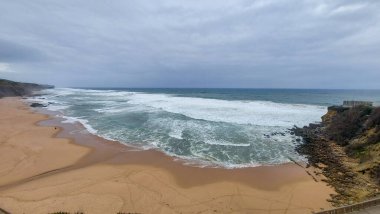 Praia do Magoito, Sintra, Portekiz - Mart 2023: Okyanus manzarası, kayalar, kum ve dalgalar sahilde. Atlantik Okyanusu 