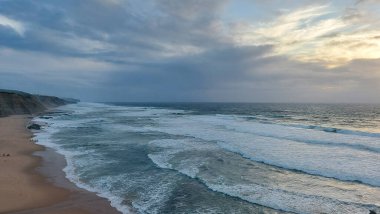 Praia do Magoito, Sintra, Portekiz - Mart 2023: Okyanus manzarası, kayalar, kum ve dalgalar sahilde. Atlantik Okyanusu 