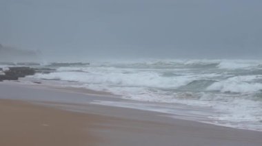 Praia do Magoito, Sintra, Portekiz - Mart 2023: Okyanus manzarası, kayalar, kum ve dalgalar sahilde. Atlantik Okyanusu.