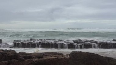 Praia do Magoito, Sintra, Portekiz - Mart 2023: Okyanus manzarası, kayalar, kum ve dalgalar sahilde. Atlantik Okyanusu.