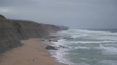 Praia do Magoito, Sintra, Portekiz - Mart 2023: Okyanus manzarası, kayalar, kum ve dalgalar sahilde. Atlantik Okyanusu.