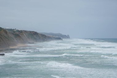 Praia do Magoito, Sintra, Portekiz - Mart 2023: Okyanus manzarası, kayalar, kum ve dalgalar sahilde. Atlantik Okyanusu