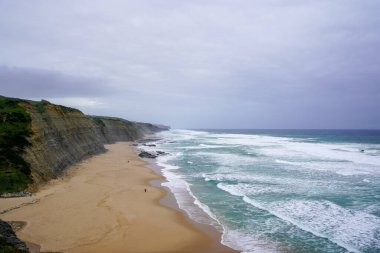 Praia do Magoito, Sintra, Portekiz - Mart 2023: Okyanus manzarası, kayalar, kum ve dalgalar sahilde. Atlantik Okyanusu