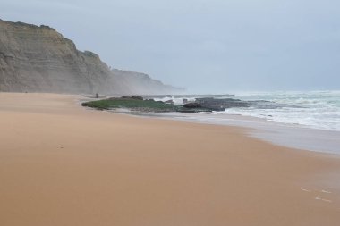 Praia do Magoito, Sintra, Portekiz - Mart 2023: Okyanus manzarası, kayalar, kum ve dalgalar sahilde. Atlantik Okyanusu