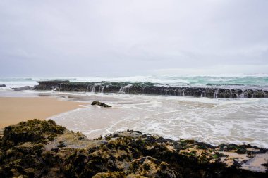 Praia do Magoito, Sintra, Portekiz - Mart 2023: Okyanus manzarası, kayalar, kum ve dalgalar sahilde. Atlantik Okyanusu