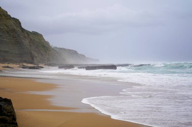 Praia do Magoito, Sintra, Portekiz - Mart 2023: Okyanus manzarası, kayalar, kum ve dalgalar sahilde. Atlantik Okyanusu
